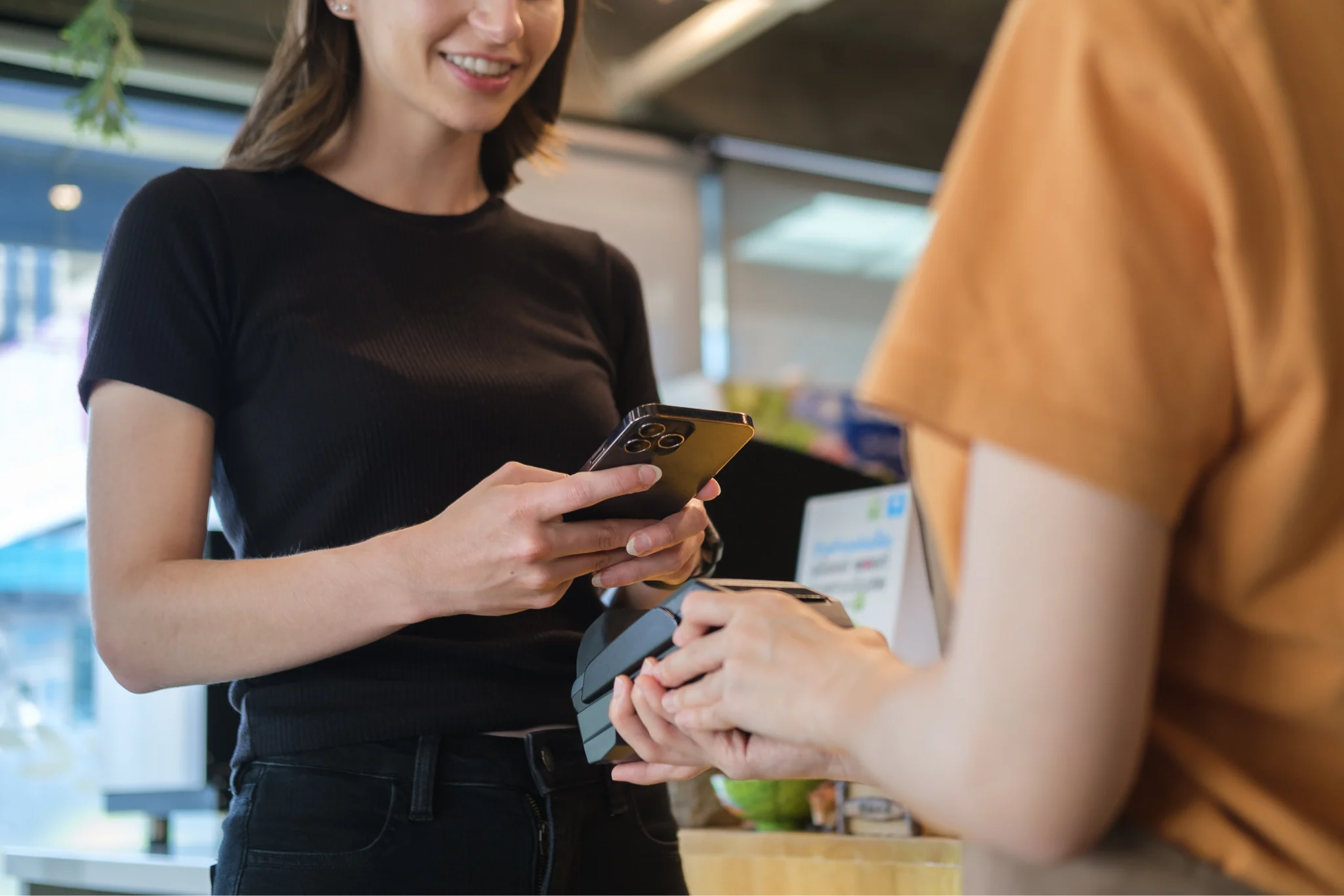 A woman using her phone to complete a checkout process on a mobile POS system held by an employee