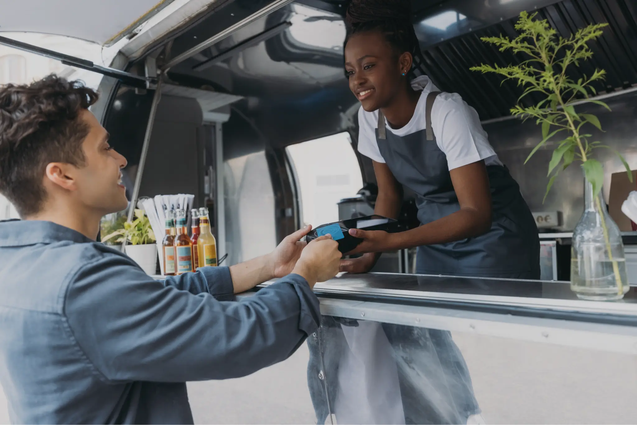 A woman working at a food truck taking a credit card from a man purchasing his food order