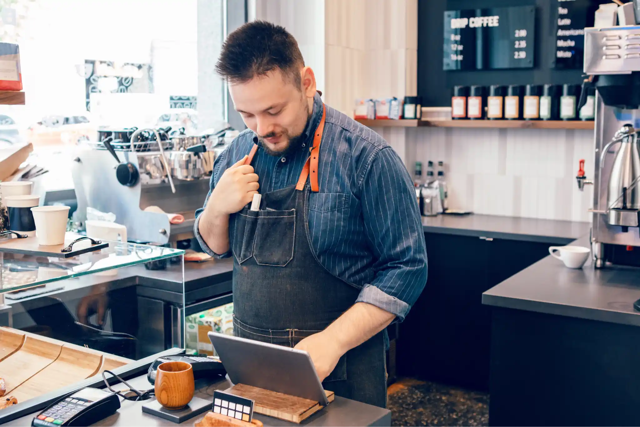 A barista in an apron using the countertop point of sale system.