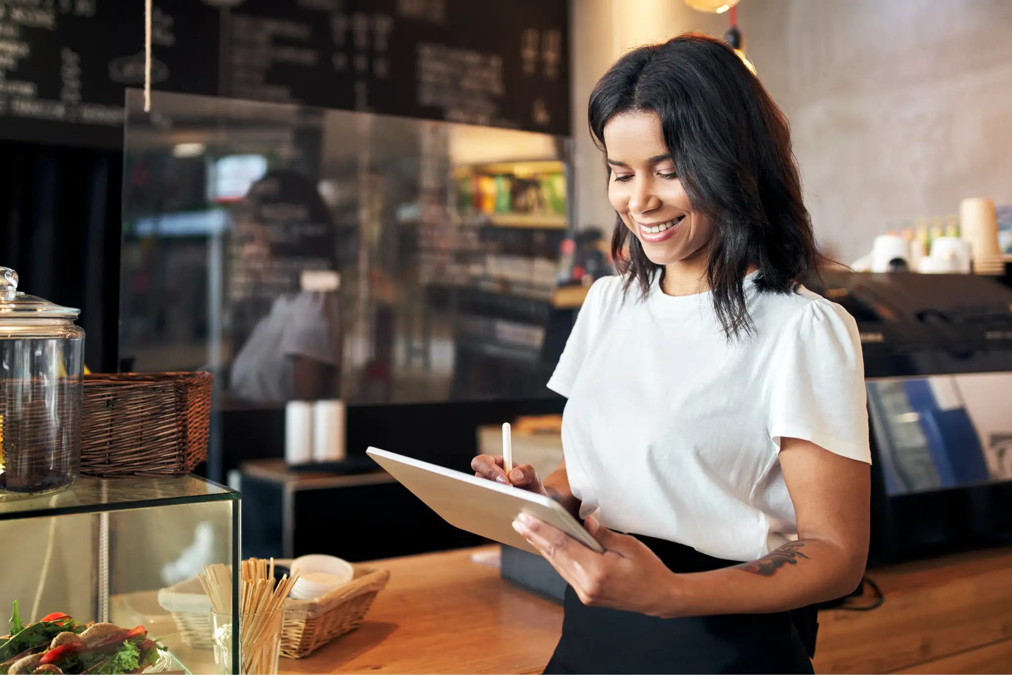 A smiling woman using her tablet with a stylus in hand.