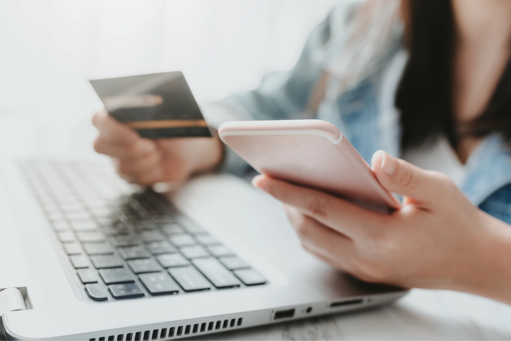 A woman holding her cell phone in one hand and credit card in the other, in front of a laptop