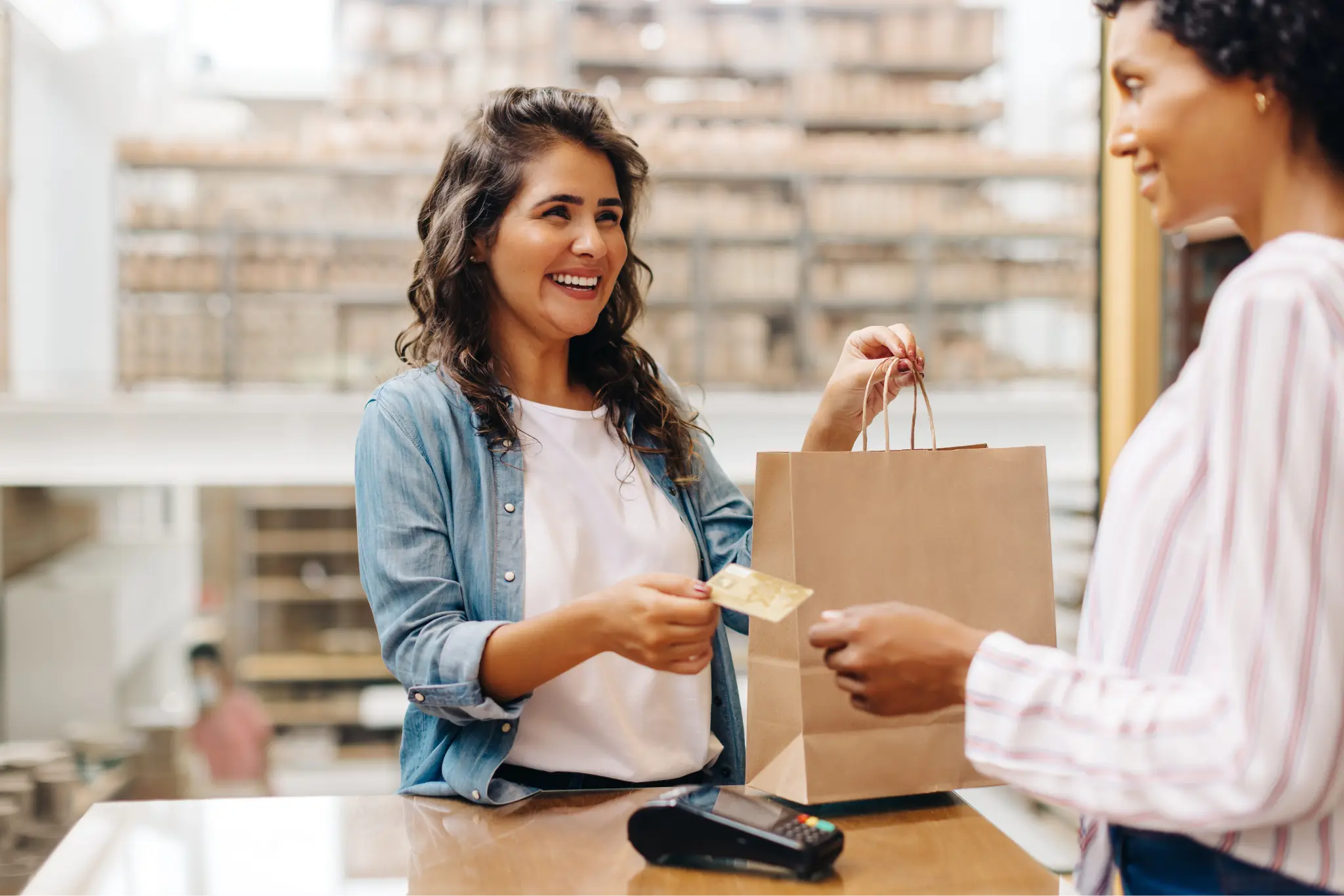 A smiling shopper her holding her bag while holding out her credit card to complete the transaction