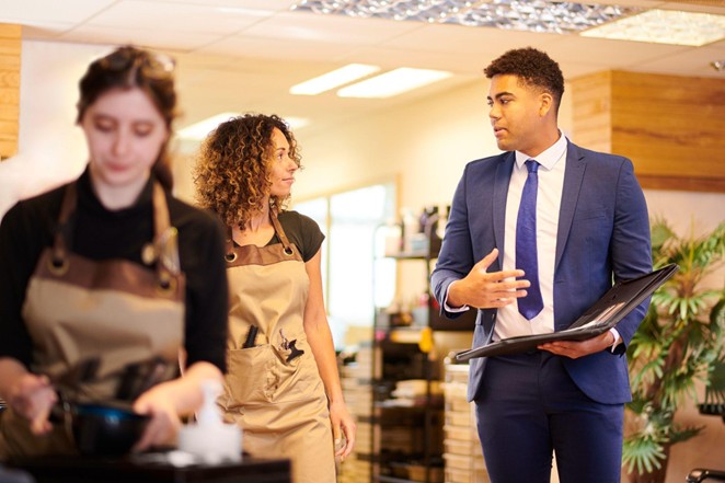 A merchant services sales agent talks to a small business owner while another person works in the foreground. 
