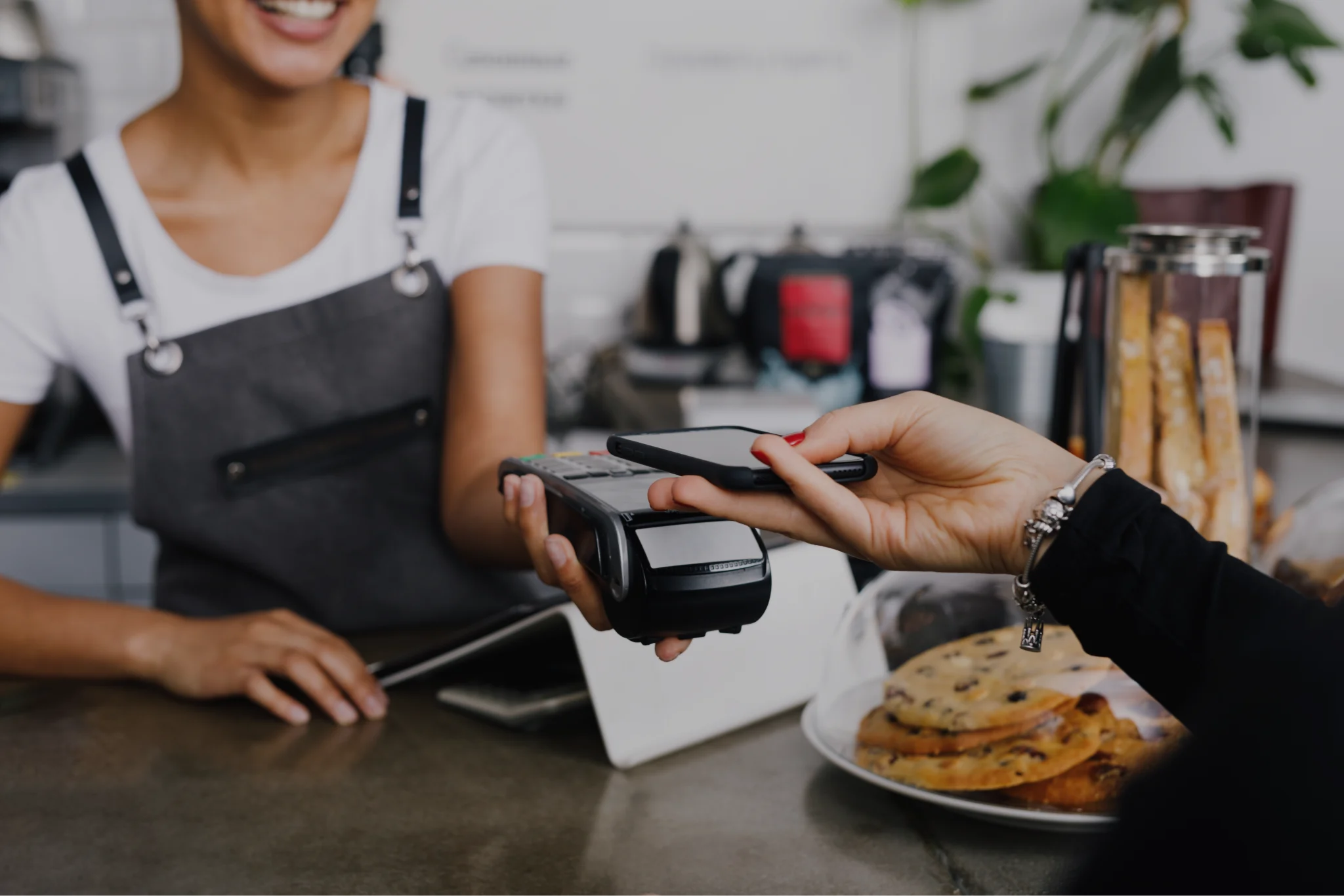 A barista holding a mobile POS system while someone holds a smart phone to it to make the purchase