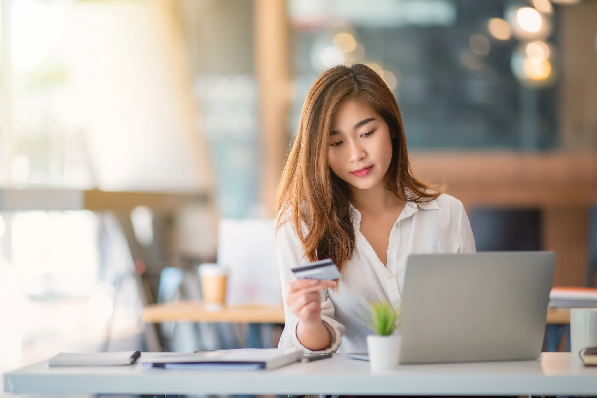 A woman sitting at a desk, holding her credit card to make a purchase on a laptop